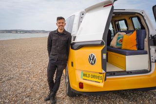 Wild Drives founder Lewis standing on the beach next to Buzz the electric campervan