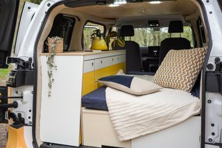 A bright yellow and white VW ID Buzz electric campervan in the woods.